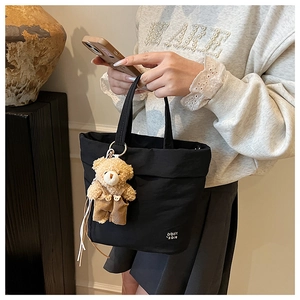 Detail of black canvas tote bag featuring a cute brown plush bear charm and white logo