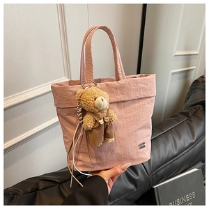 Detail of pink pleated tote bag featuring a cute plush bear charm and metallic logo