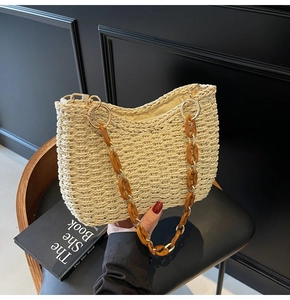 Detailed close-up of straw woven bag featuring amber acrylic and gold metal chain strap