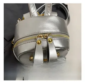 Close-up of golden dual zippers and rivet details on silver metallic leather backpack