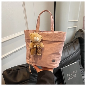 Detail view of pink pleated tote bag with teddy bear charm on a leather sofa