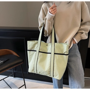 Detail of light green canvas tote bag with black trim and convenient front pockets