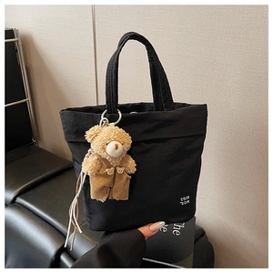 Detailed shot of black minimalist tote bag with cute plush bear pendant and thick handles