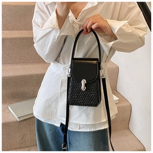 Detail of a black crossbody bag with woven texture and silver metal clasp on a model