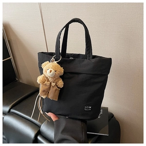 Detail of black nylon tote bag featuring a cute plush bear charm and white logo text