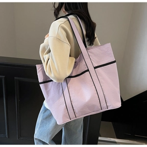 Detail of light purple tote bag with black trim worn on shoulder by a model