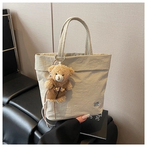 Close-up of minimalist beige tote bag with metallic logo and cute brown teddy bear charm