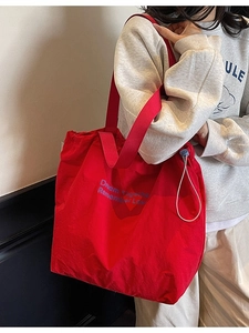 Minimalist red drawstring tote bag with blue typography print and adjustable shoulder strap