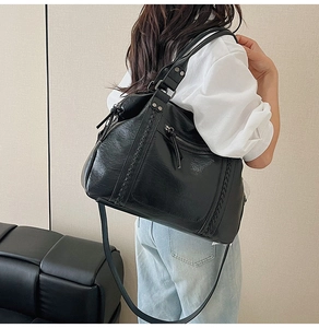 Close-up of black leather tote bag with woven details and silver zippers on back of model