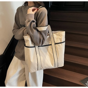 Detail of a large beige tote bag with black piping and textured fabric on wooden stairs