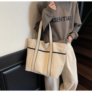 Detail of a large cream canvas tote bag with black contrast trim on a shoulder strap