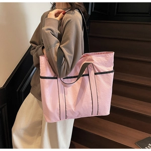 Pink large capacity tote bag with black trim and side pocket on a model in a stairwell