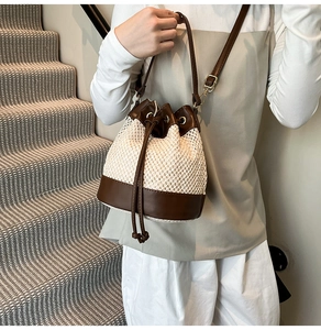 Detail of a woven bucket bag with leather base and drawstring closure shown on a model