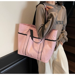 Detail of pink nylon tote bag showing side storage pocket and black webbing handles