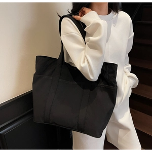 Detail view of large black tote bag with side pocket on shoulder of a model in white hoodie