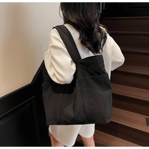 Side view of a black large-capacity tote bag worn by a model on a wooden staircase