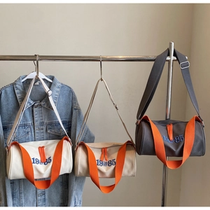 Détails des sacs cylindriques en toile blanche, beige et grise avec poignées orange vif
