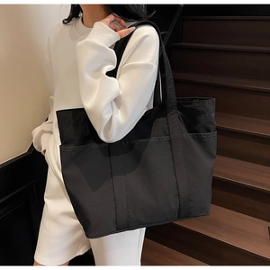 Detail view of a large black tote bag featuring multiple external storage pockets