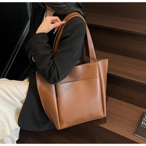 Close-up of a large brown tote bag with front pocket shown in a professional work setting