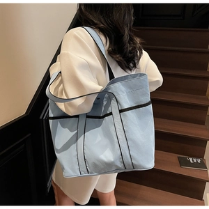 Detail view of large sky blue tote bag with black strap accents on a shoulder model
