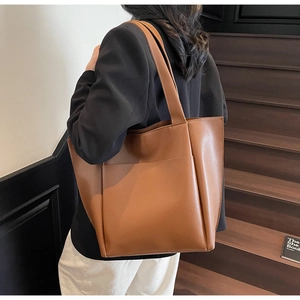 Detail view of the brown leather tote bag showing a large front pocket and smooth texture