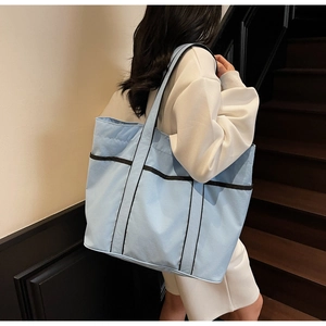 Side view of light blue tote bag with black trim and webbing handles worn by a model