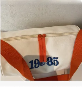 Détail des doubles fermetures éclair et de la broderie bleue 1985 EST sur sac en toile