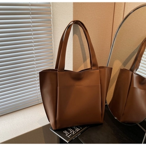 Detail of a large brown faux leather tote bag with front pocket in a city lifestyle setting
