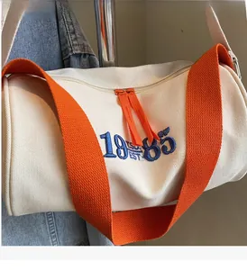 Détail du sac baril en toile avec broderie 1985 bleue et bandoulières orange vif