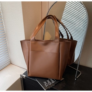 Detail of a brown faux leather tote bag showing wide handles and a large front pocket