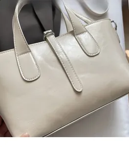 Detailed close-up of cream textured leather bucket bag with metallic ring and fine stitching