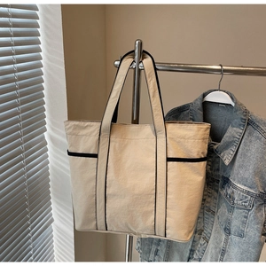 Detail of a large beige canvas tote bag with black trim hanging on a metal hanger
