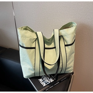 Detail of light green tote bag featuring black contrast trim and sleek shoulder straps