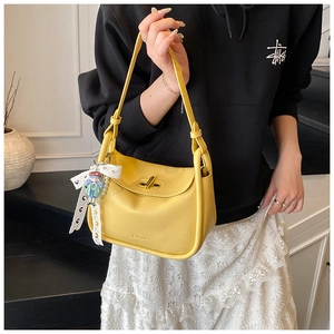 Detail of yellow lychee leather bag featuring a gold clasp and lace butterfly charm