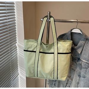 Detail of mint green tote bag with contrast black straps hanging in natural light