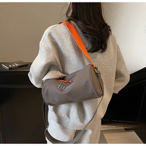Détail d'un sac de sport cylindrique gris avec des anses orange et une broderie