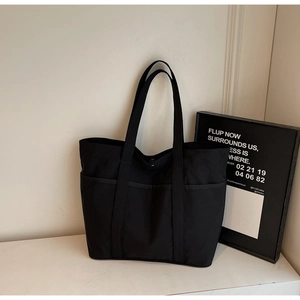Close-up of a large black tote bag featuring two functional front pockets and wide handles