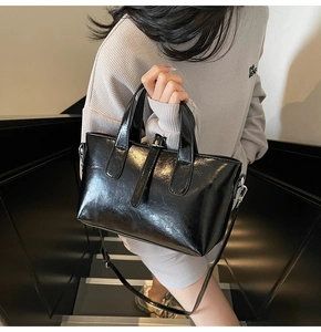 Detail of a black glossy patent leather trapezoid handbag with handles and shoulder strap