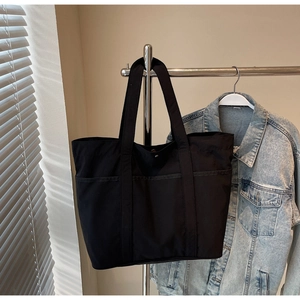 Detail of black large capacity tote bag with three front pockets on a metal rack
