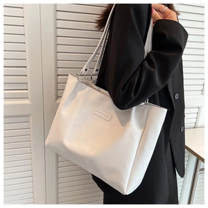 Detail view of a white textured leather tote bag featuring thin straps and fashion text logo