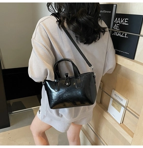 Chic black patent leather bucket bag with a top handle and shoulder strap shown on a model