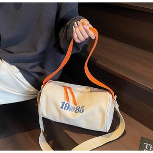 Détail d'un sac cylindre en toile rétro avec broderie 1985 et poignées orange