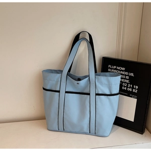 Detail of light blue canvas tote bag with black strap accents and metal snap button closure