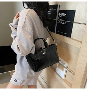 Detail view of a black glossy leather handbag featuring a sleek buckle and adjustable strap