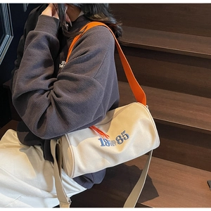 Détail du sac cylindre en toile crème avec broderie 1985 et bandoulière orange vif