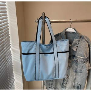 Detail of light blue tote bag with black strap accents and metal snap button closure