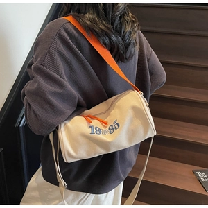 Détail du sac cylindrique en toile avec broderie bleue et bandoulière orange vif