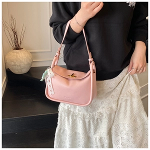 Detail of pink lychee leather handbag with golden lock and lace accessory on a model