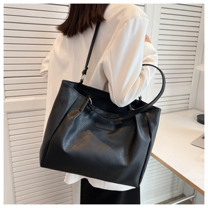 Detailed view of black tote bag featuring litchi texture and fashion logo plaque