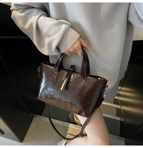 Detail of a dark brown glossy leather tote bag with top zipper and adjustable strap